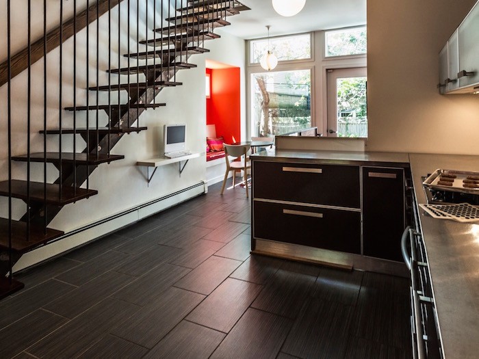 Dark modern kitchen. Small with hallway and modern stairs. Bright orange sitting area.